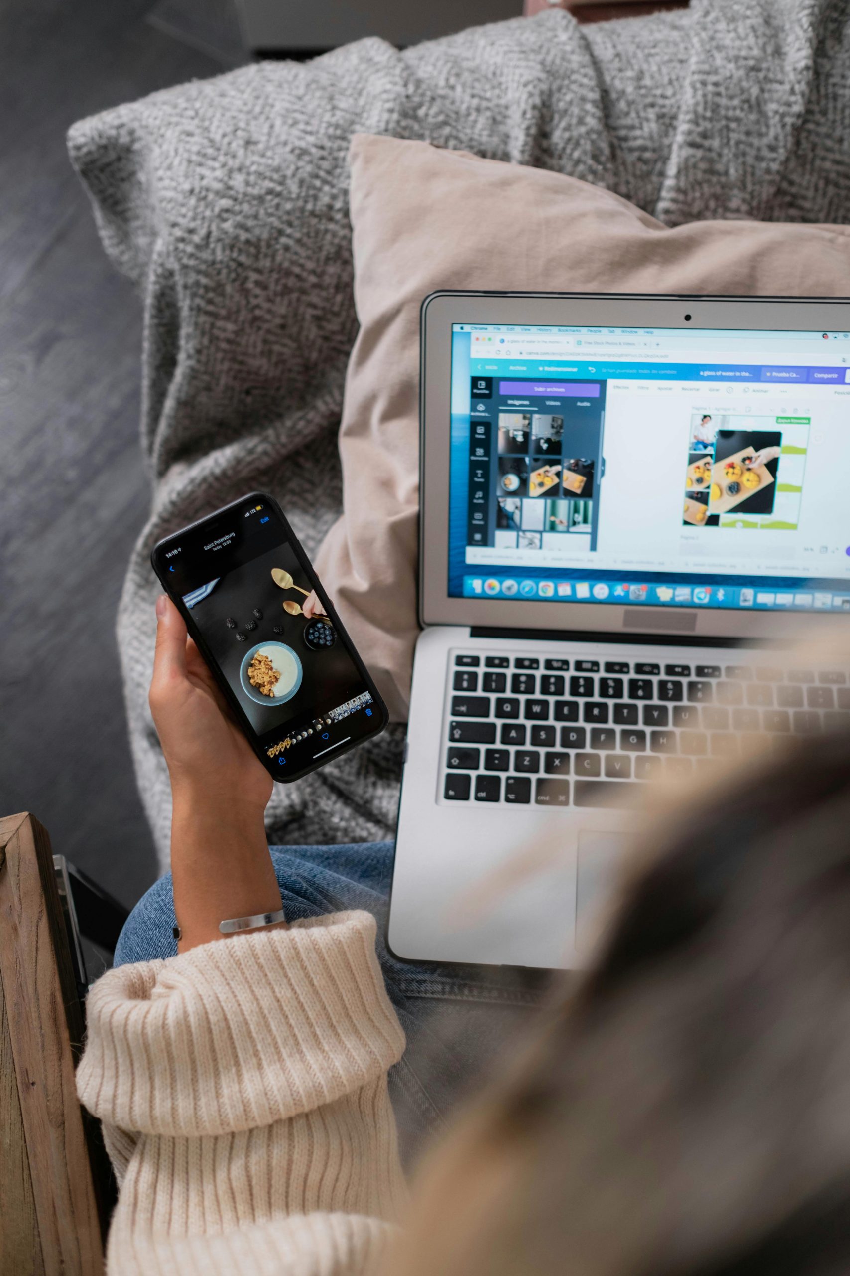 Ordinateur portable sur les genoux, téléphone mobile dans la main, une personne fait sa mise en page sur Canva