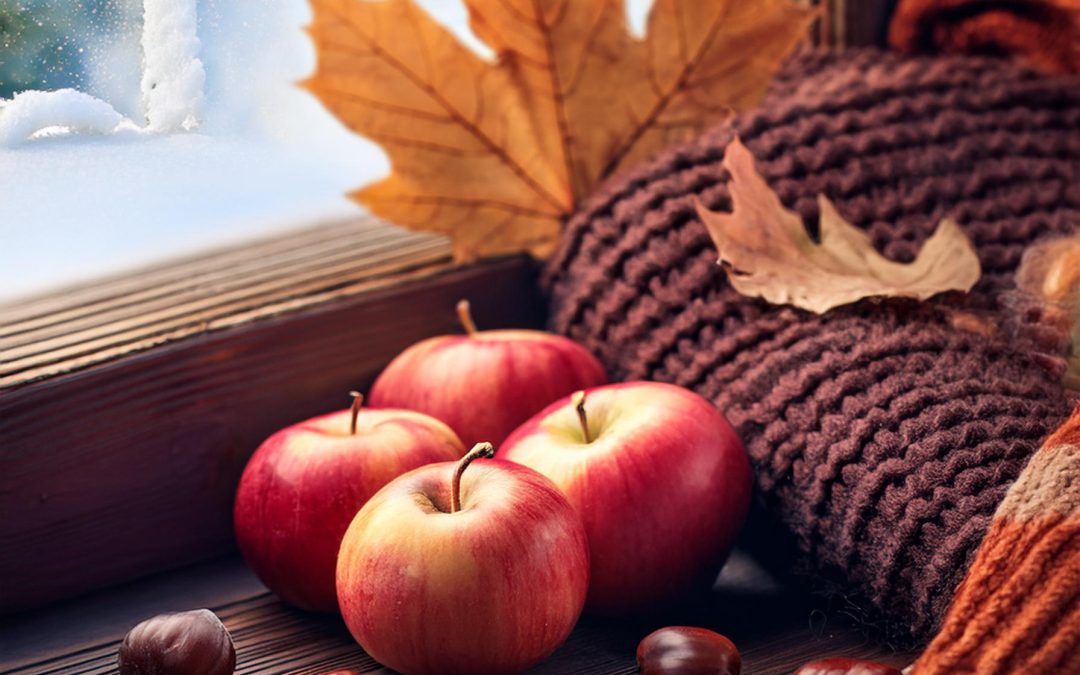 Pommes rouges, feuilles d'automne posées sur le bord d'une fenêtre avec un pull et une écharpe. On devine le froid à l'extérieur.