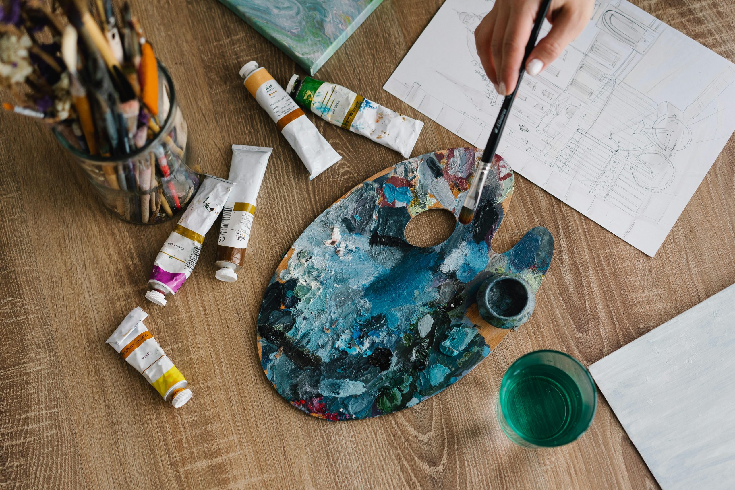 pexels-mikhail-nilov-6932377 Palette à dessin avec tubes de couleur, on y aperçoit une main qui tient un pinceau